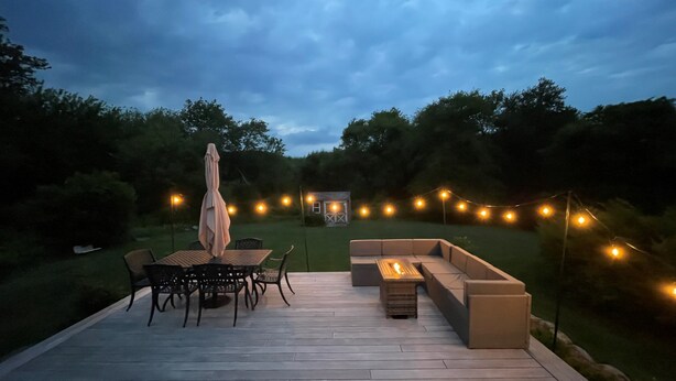 Una terraza al aire libre con zona de comedor, fogata y luces colgantes.