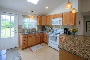 A kitchen with wooden cabinets, a microwave, a stove, and pendant lighting. - Large Contemporary Home, Walk to Beach Central Air Conditioning, Spacious Deck (Narragansett)
