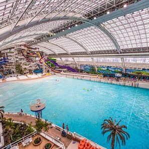 Ein großer Indoor-Wasserpark mit einem Schwimmbecken, mehreren Wasserrutschen und einer hohen, gläsernen Deckenkonstruktion.