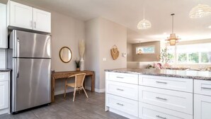 Eine moderne Küche mit weißen Schränken, einem Edelstahlkühlschrank, einem Holztisch und Pendelleuchten.