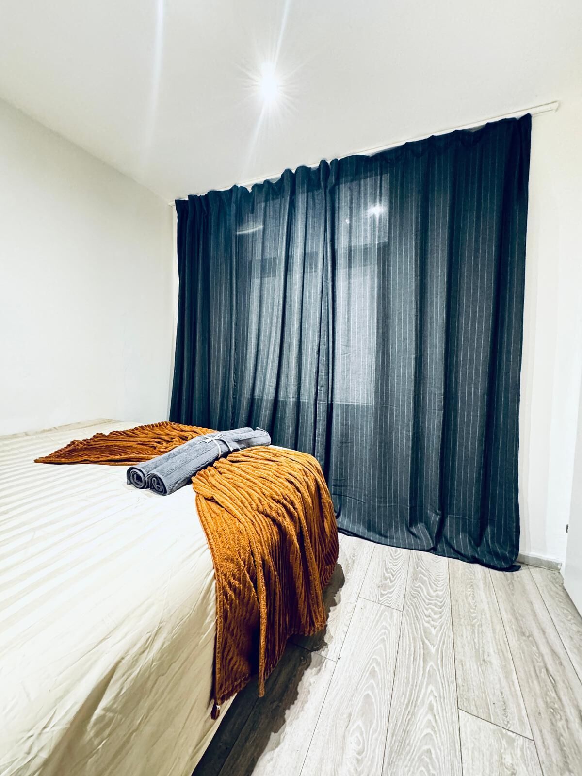 Una camera da letto con un letto, tende scure e pavimento in legno.