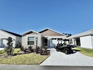 Een rij gelijkvloerse huizen met aangebouwde garages, een verharde oprit en een klein gazon.