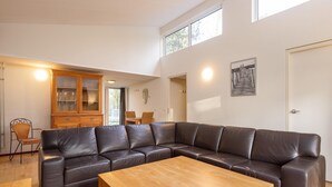 A modern living room with a leather sectional sofa, a wooden coffee table, and a dining area with a chair and cabinet. - Beautiful bungalow at the Kootwijkerzand. (Kootwijk)