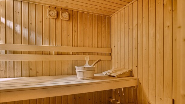 Una sauna de madera con bancos, un cubo y una cuchara, y dos relojes de pared.