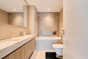 Une salle de bain moderne avec un grand miroir, un meuble-lavabo à deux vasques, une baignoire et des toilettes.