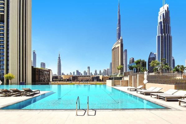 Une piscine sur le toit, agrémentée de chaises longues, offrant une vue sur le paysage urbain de Dubaï et sur le Burj Khalifa.