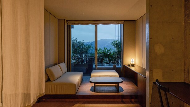 A modern room with a sofa, a small table, and a view of mountains through large windows. - KÚON Hakone Gora (Hakone)