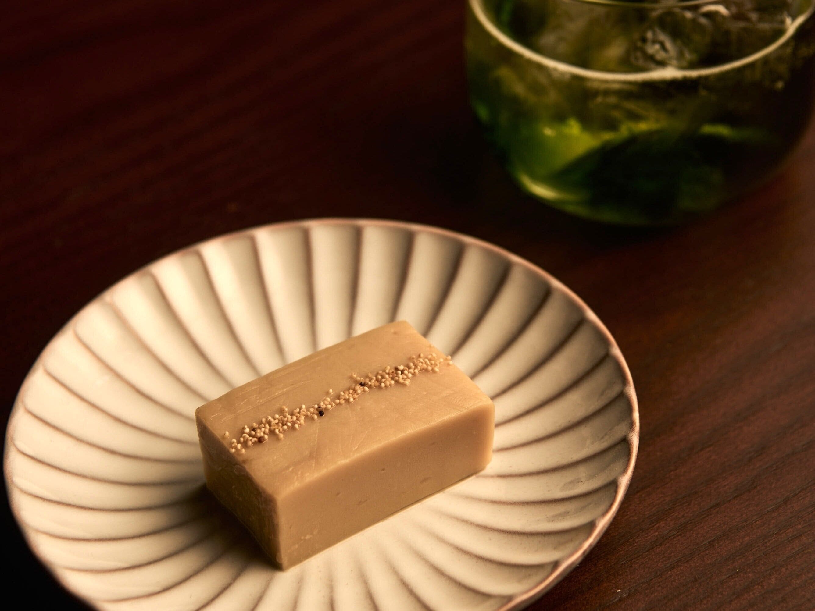 A rectangular bar of soap on a white plate with a ribbed edge, placed on a wooden surface.