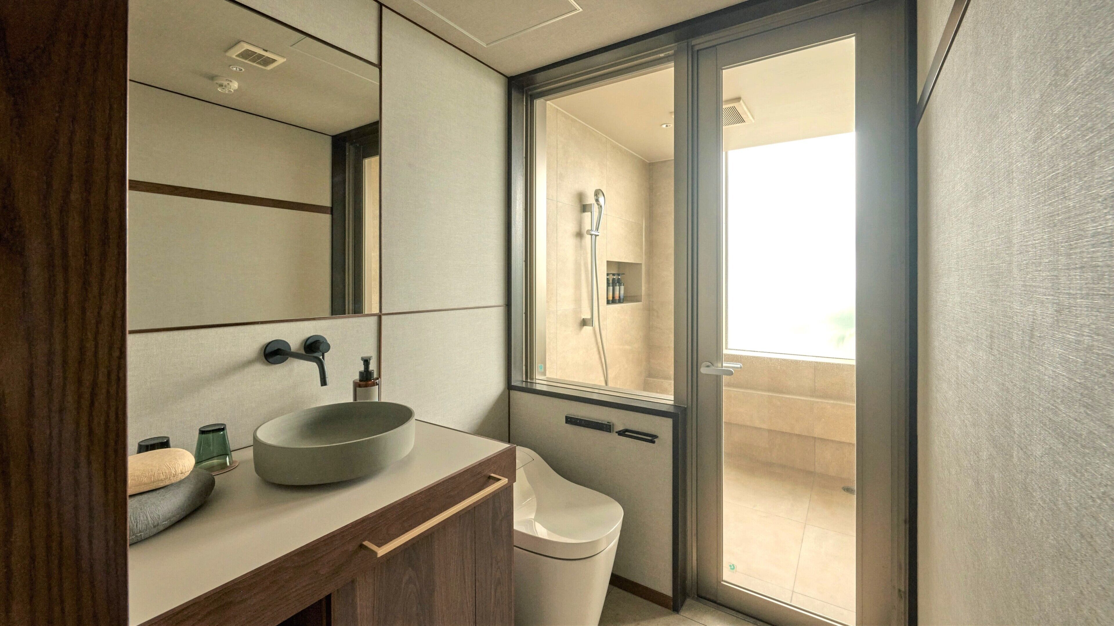 A modern bathroom with a large mirror, a vessel sink, a toilet, and a shower area visible through a glass door.