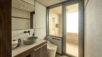 A modern bathroom with a large mirror, a vessel sink, a toilet, and a shower area visible through a glass door.