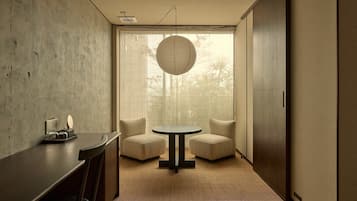 A modern room with a round table, two chairs, a concrete wall, and a large window with a view of trees.