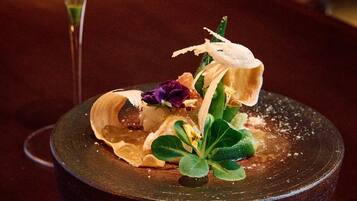 A dessert with a dark plate, green leaves, and purple flowers.