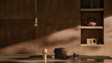 A minimalist kitchen with a hanging light, a pot, a teapot, and a shelf with decorative items.