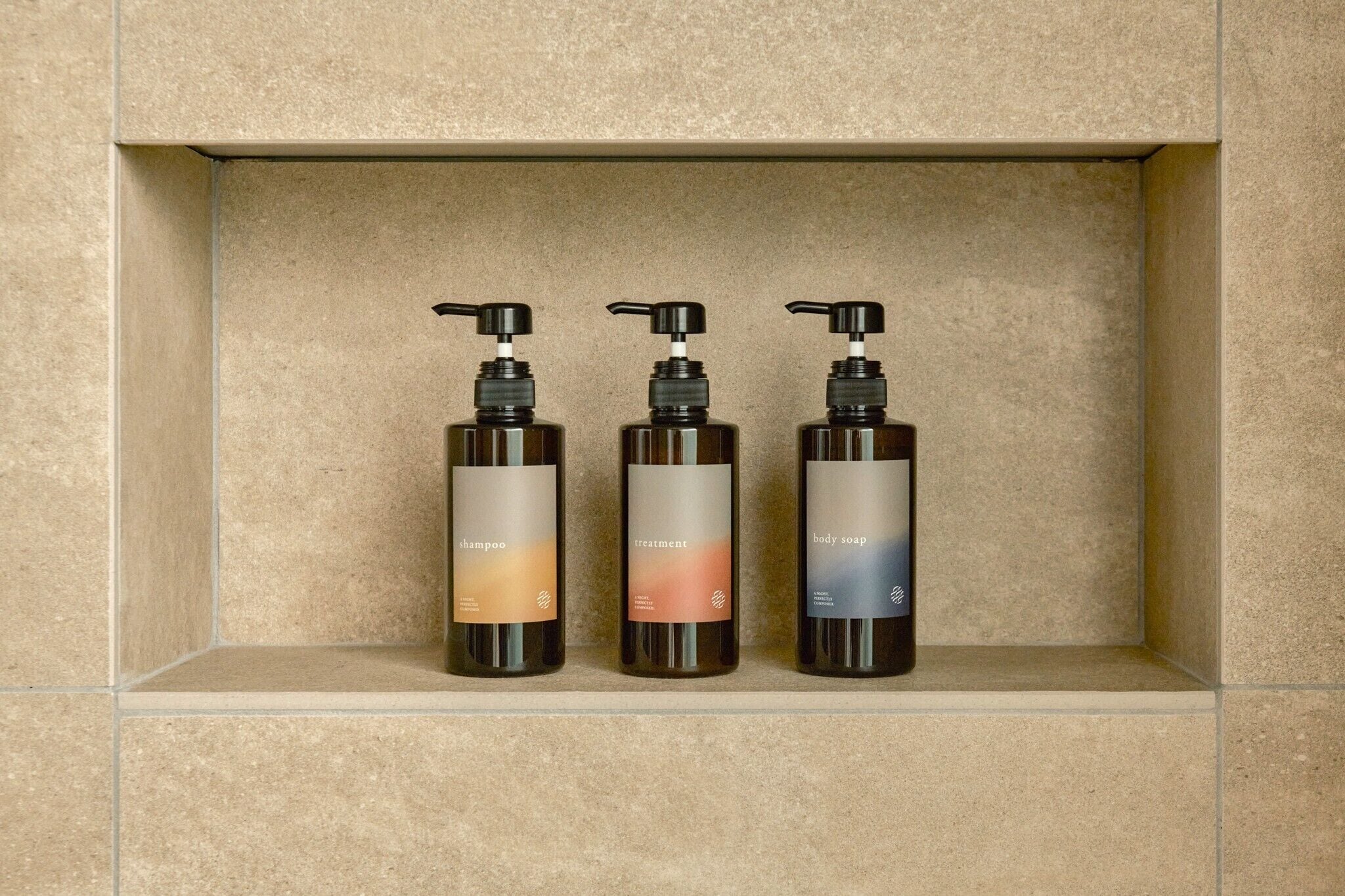 Three bottles of shampoo, treatment, and body soap on a shelf.