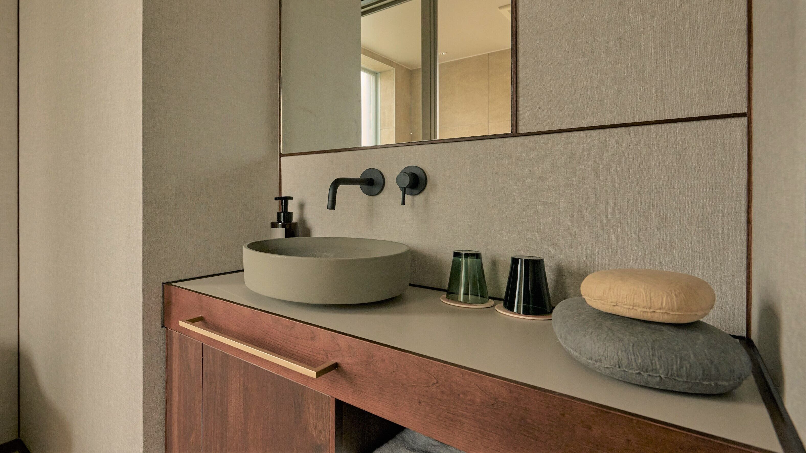 A bathroom with a round sink, a mirror, a towel, and a small stool.