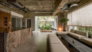 A modern interior with a stone counter, a seating area with a sofa and a bench, and a view of a garden through large windows. - KÚON Hakone Gora (Hakone)