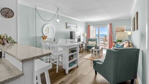 Amplia sala de estar con una mesa de comedor, sillas, un sofá y vistas al exterior.