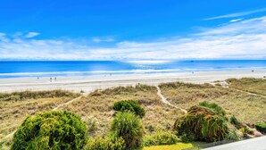 Una playa con cielo despejado, orilla arenosa y algo de vegetación al frente.