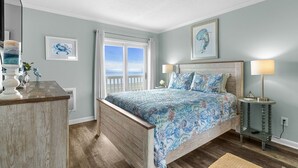 Un dormitorio con cama, lámparas de noche, cómoda y vista al océano.
