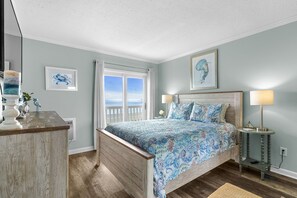 Ein Schlafzimmer mit Bett, Nachttischlampen, einem Schminktisch und Blick aufs Meer.