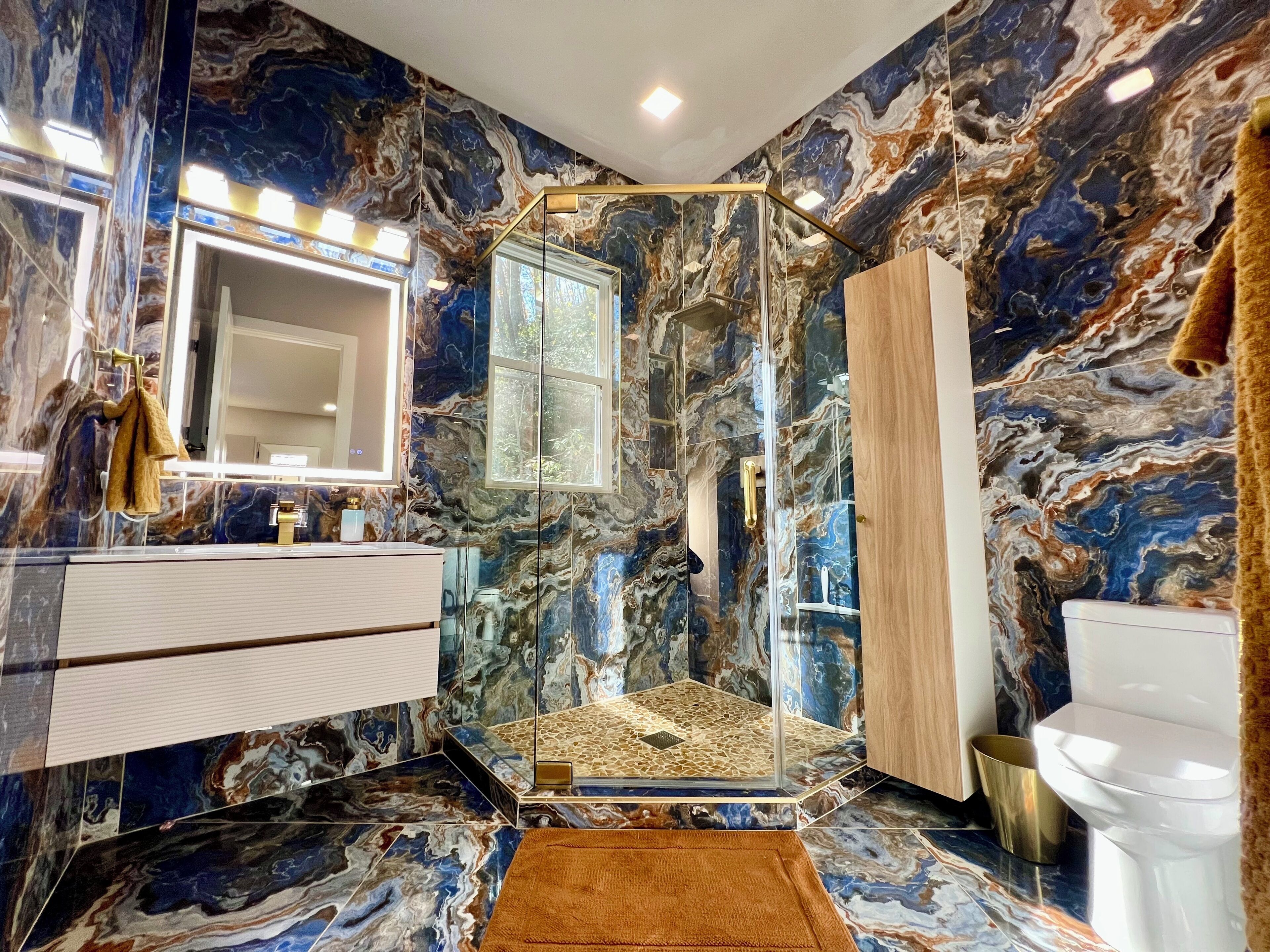 Une salle de bain avec un mur en marbre, une douche en verre, des toilettes blanches et un meuble en bois.