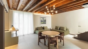 Un salon moderne avec un plafond en bois, une table de salle à manger ronde entourée de chaises, un canapé vert et un tableau accroché au mur.
