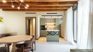 Un intérieur moderne avec un plafond en bois, un coin repas comprenant une table ronde et des chaises, une cuisine dotée d’un îlot central et de grandes fenêtres avec des rideaux.