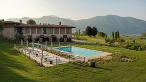 Un espace piscine doté de chaises longues et de parasols, entouré d’une pelouse bien entretenue et offrant une vue sur les montagnes.
