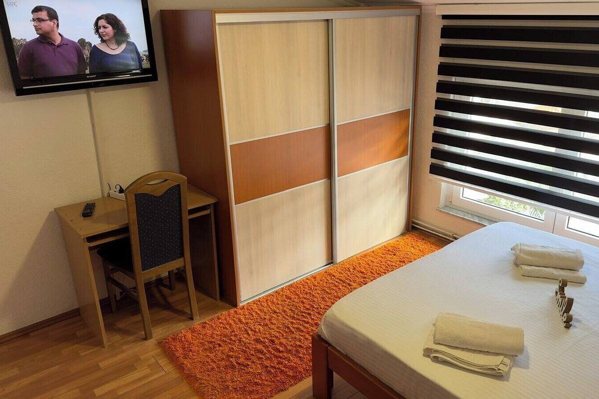 A hotel room with a bed, a desk, a chair, a wardrobe, and a TV mounted on the wall.