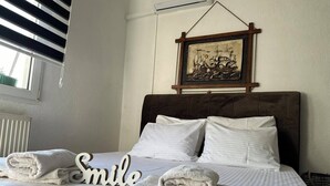 Una cama bien hecha con sábanas blancas y toallas dobladas, un cuadro enmarcado encima y una ventana con persianas.