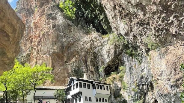 Un edificio blanco de varios pisos, ubicado al borde de una piscina azul cristalina, rodeado de acantilados rocosos.