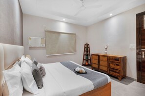 A bedroom with a bed, bedside table, dresser, and a ceiling fan. - Alaya Stays Krishna Manor 3BHK With Pool (Noida)