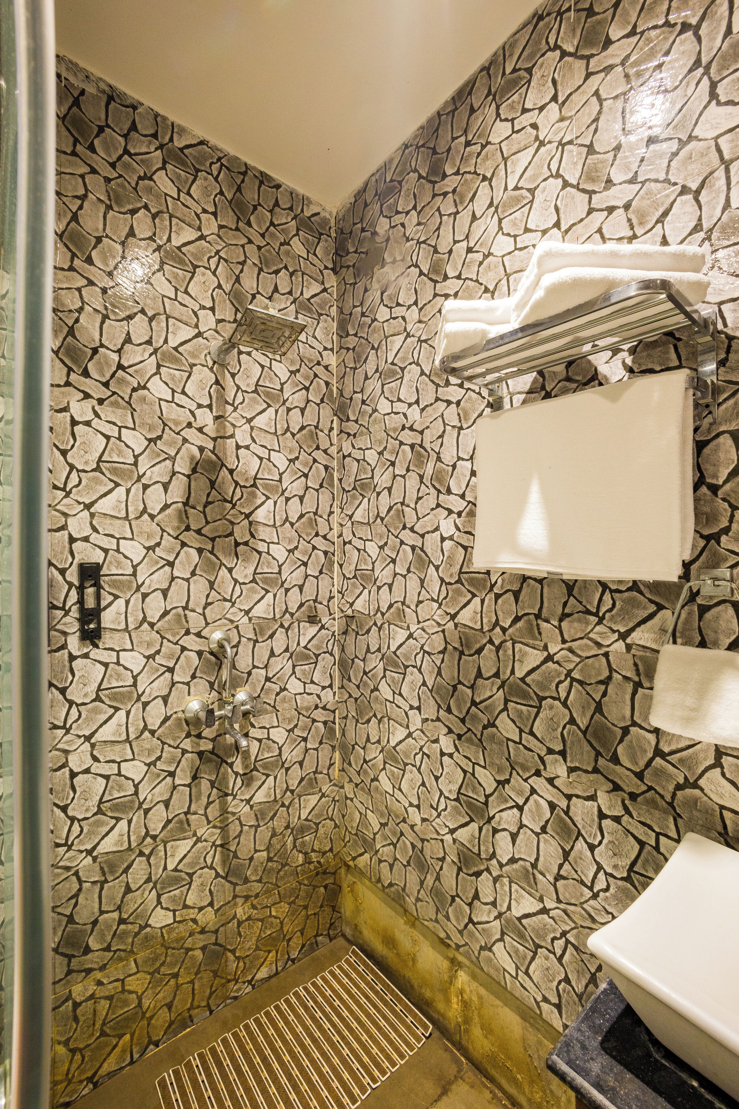 A bathroom with a stone mosaic wall, a shower, a sink, and a towel rack.