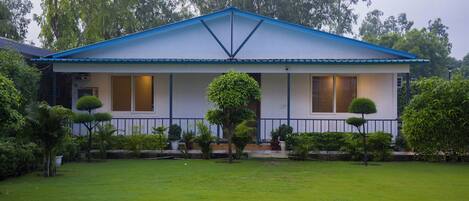 A two-story house with a blue roof and white walls, surrounded by a well-maintained lawn and various shrubs.
