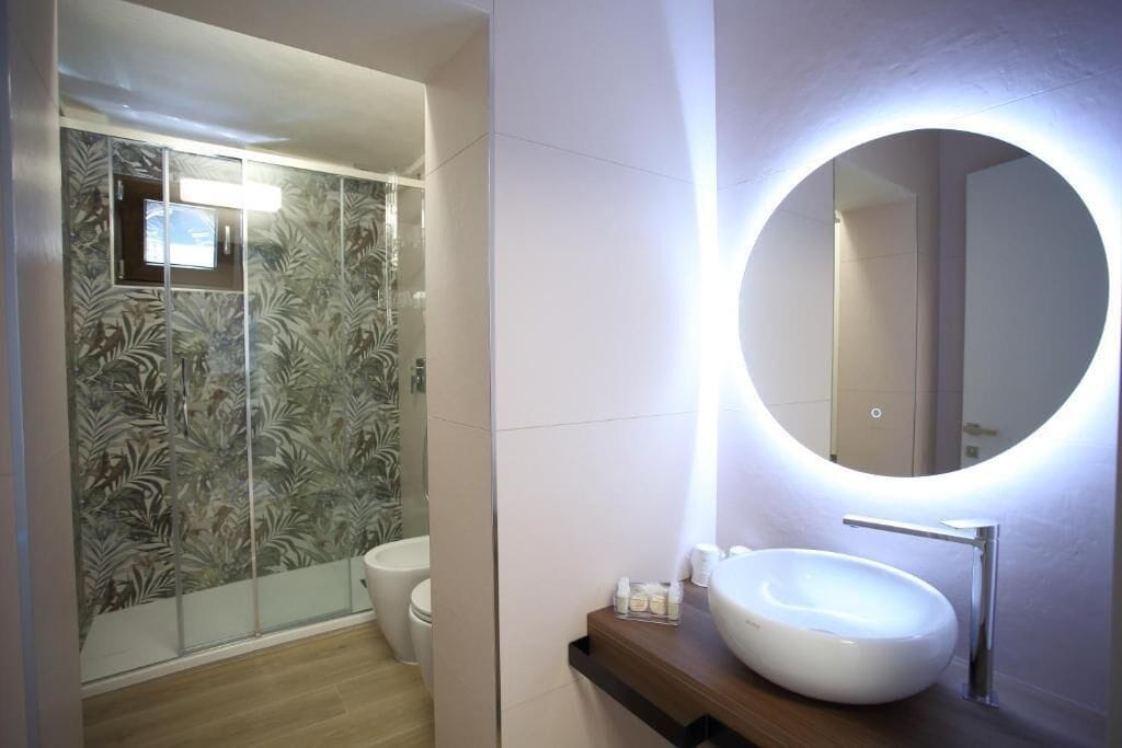 Un bagno con uno specchio tondo, un lavandino bianco e un box doccia in vetro.