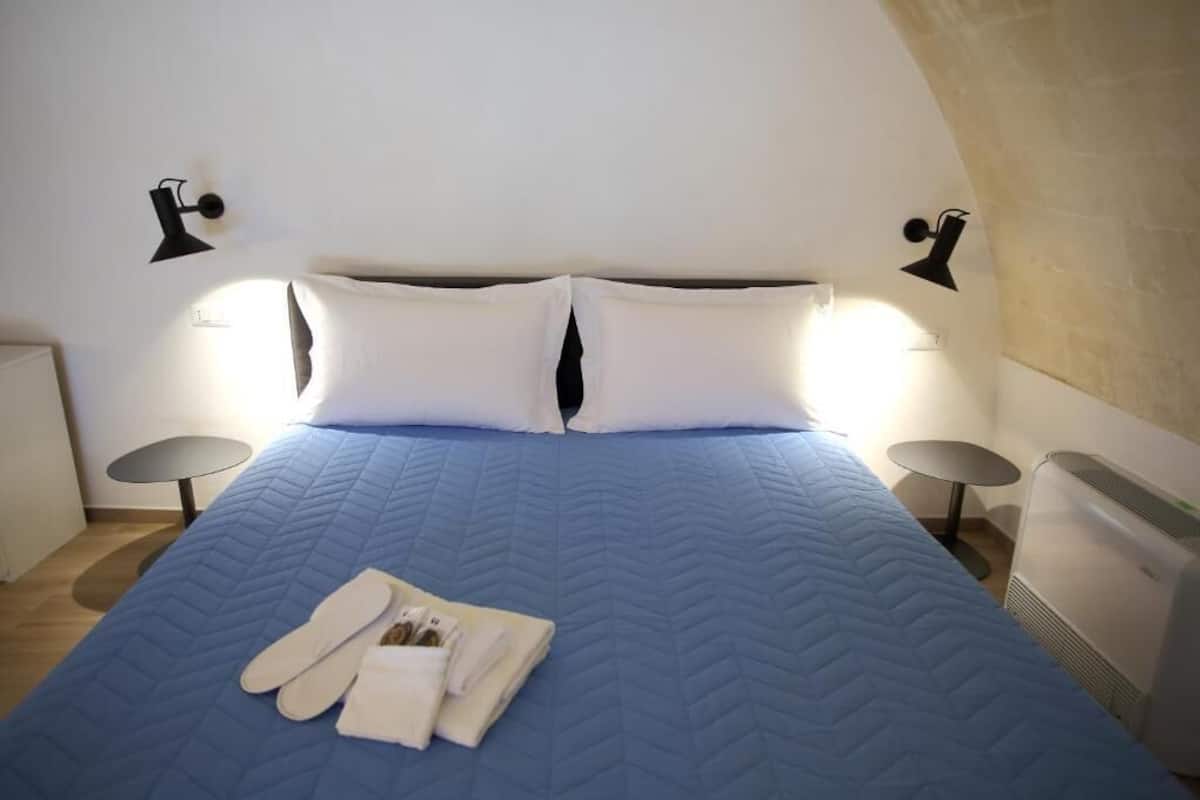 A hotel room with a large bed, two bedside tables, and a heater.