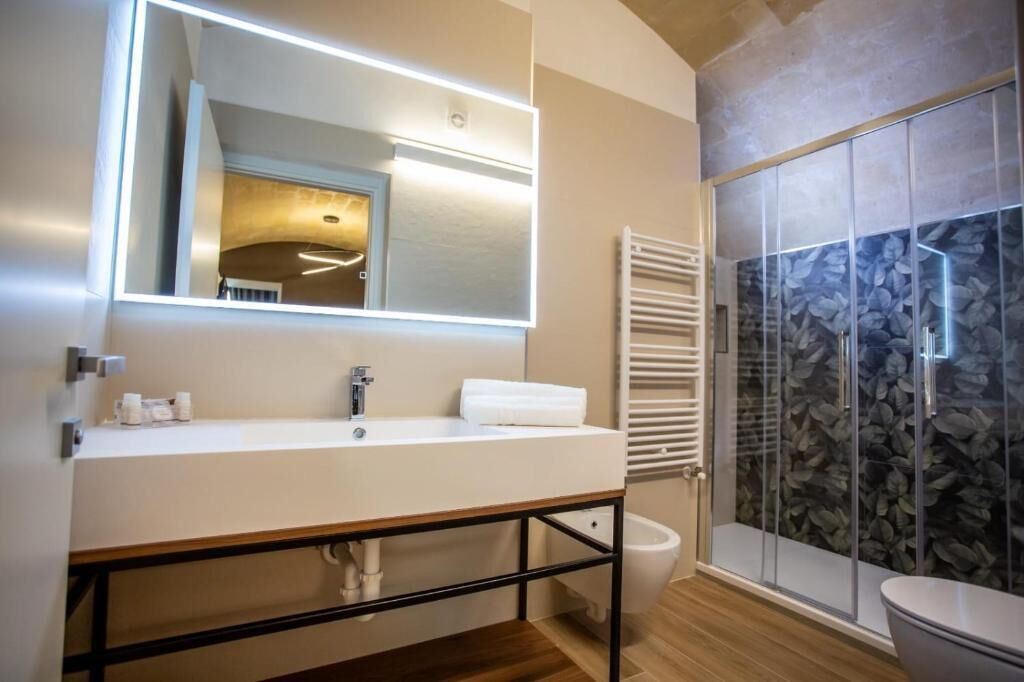 Un baño moderno con un espejo grande, un lavamanos blanco, una toalla, una ducha con pared de piedra y un inodoro.