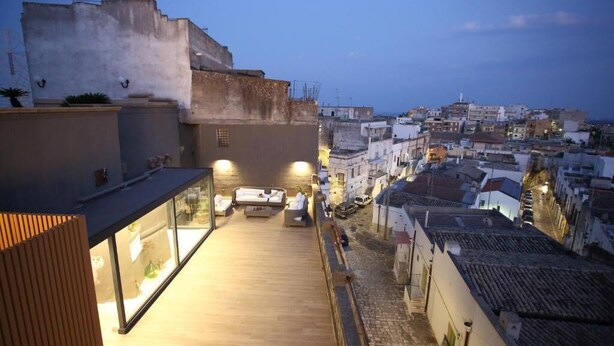 Una terraza en la azotea con mobiliario exterior y vistas a la ciudad al anochecer.