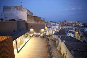 Una terraza en la azotea con mobiliario exterior y vistas a la ciudad al anochecer.
