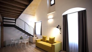 Una sala de estar moderna con un sofá amarillo, sillas blancas, una mesita y una escalera.