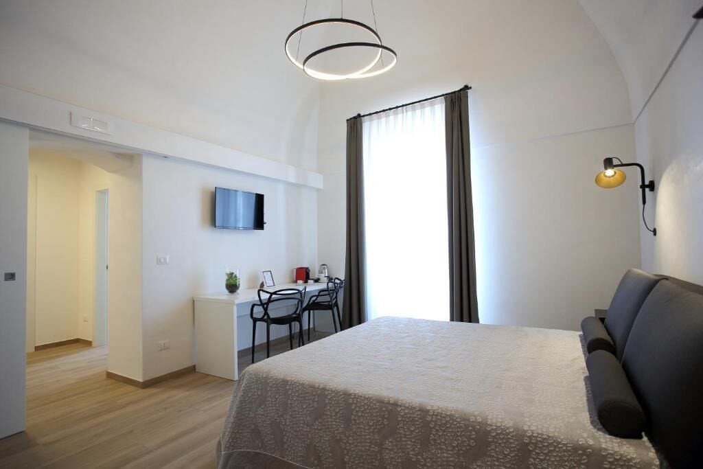A modern hotel room with a large bed, a desk with chairs, a TV, and a window with curtains.