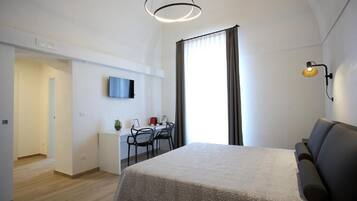 A modern hotel room with a large bed, a desk with chairs, a TV, and a window with curtains.