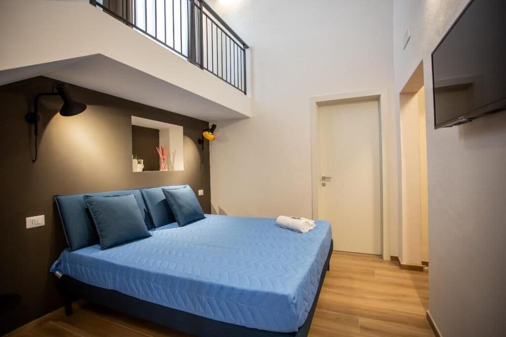 A bedroom with a bed, a small balcony, a TV, and a door.