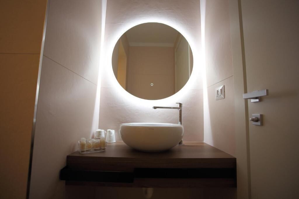 A bathroom with a round mirror, a white sink, and a light fixture above the mirror.