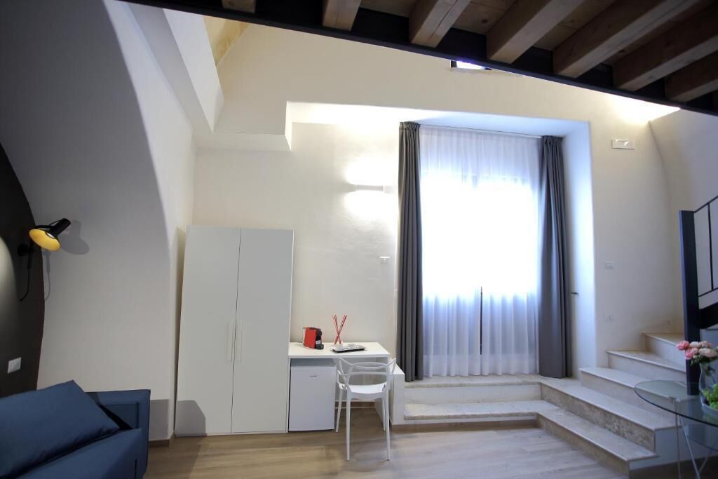 Un ambiente compatto con scrivania, sedia e un angolo cottura. Una scala conduce a un livello superiore.