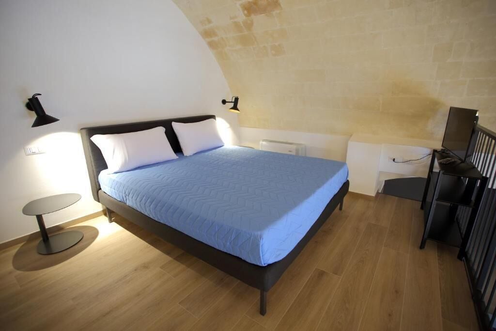 Un dormitorio con cama, mesitas de noche, un escritorio y una lámpara.