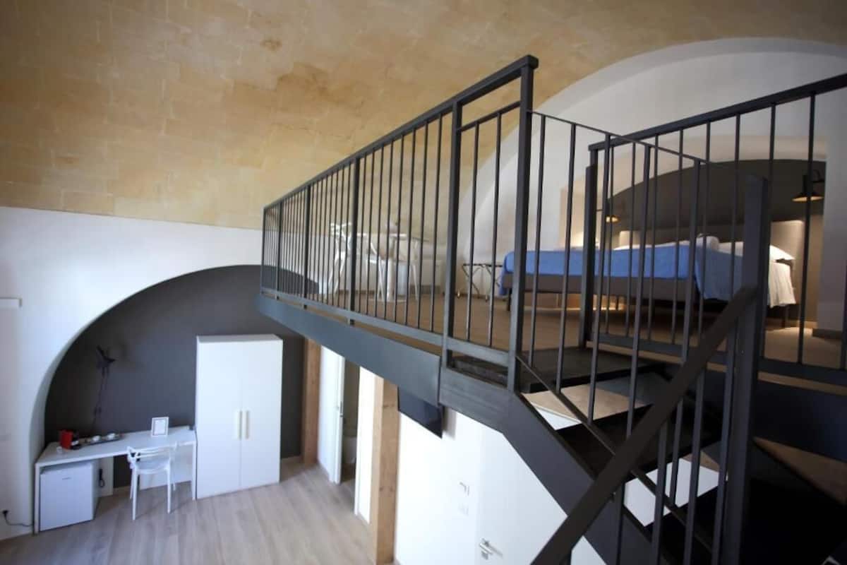 A modern loft bedroom with a mezzanine, a desk, and a chair in the lower level.