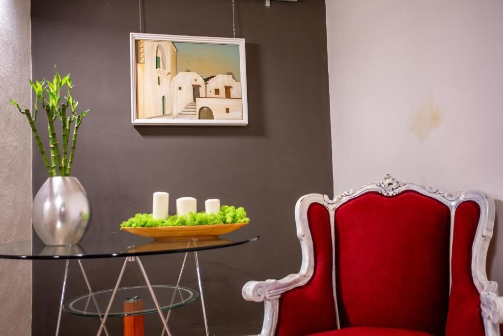 Una habitación con una mesa de vidrio, una silla roja, un jarrón con plantas verdes y un cuadro en la pared.