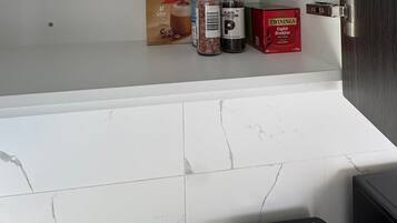 A kitchen with a white tiled backsplash, a toaster, and a shelf with a Nescafé cappuccino pack, black pepper, and Twinings English Breakfast tea.