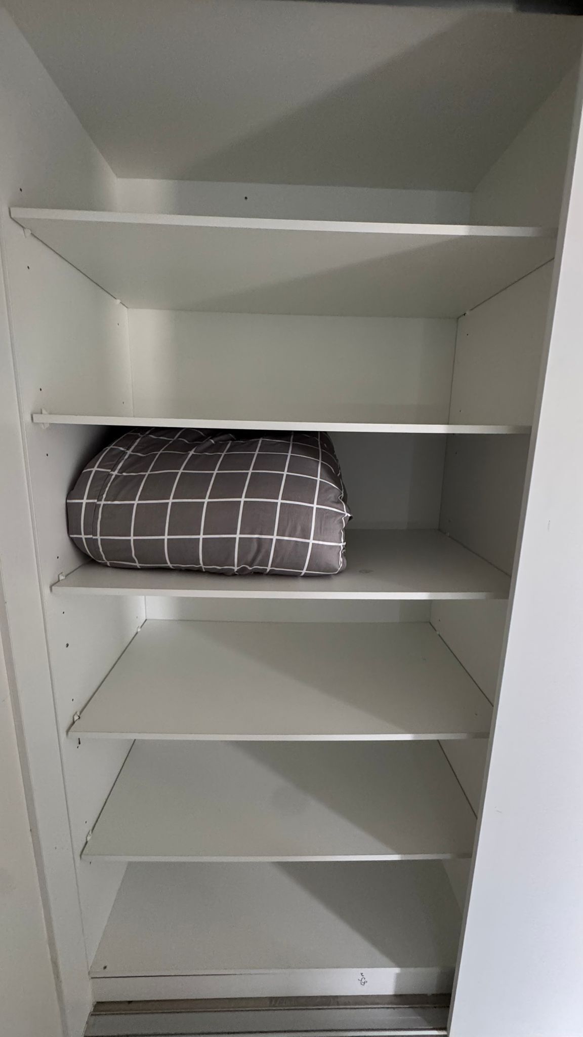 A white closet with three shelves, one of which holds a black and white checkered pillow.
